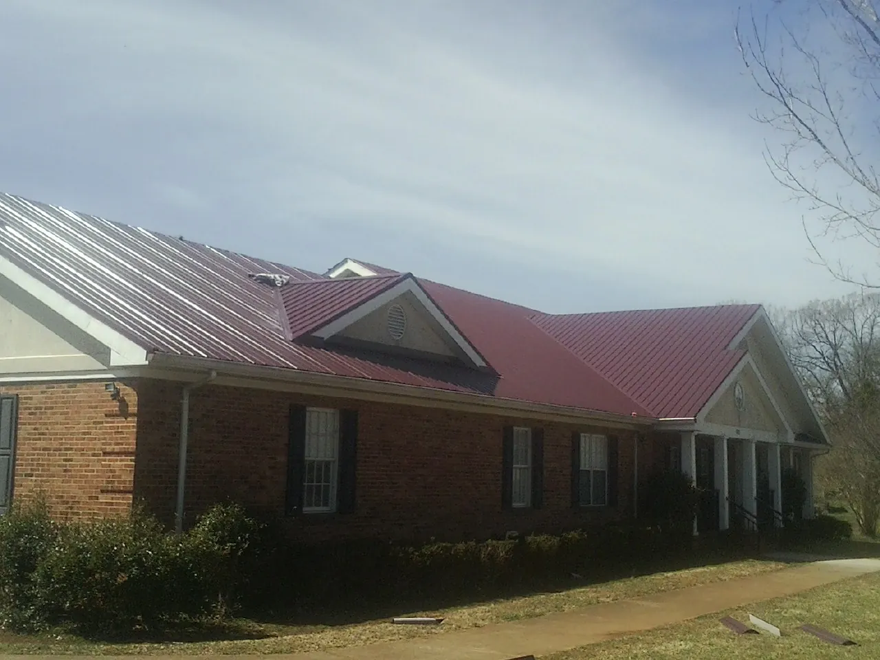 Red metal roof with gabled entries on a long brick building, from a Hail Damage Roof Repair job in Silverton
