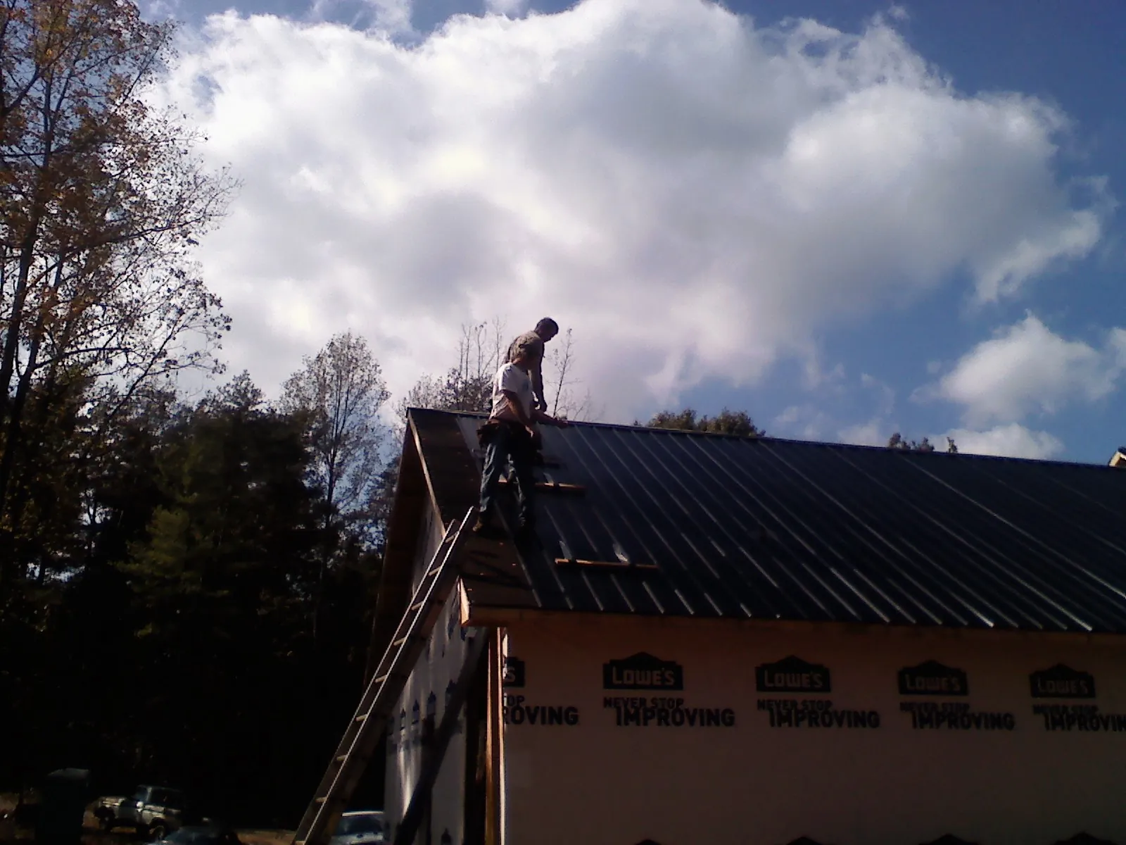 Roofer fastening dark metal panels high against a cloudy sky, from a Roof Inspection job in Silverton