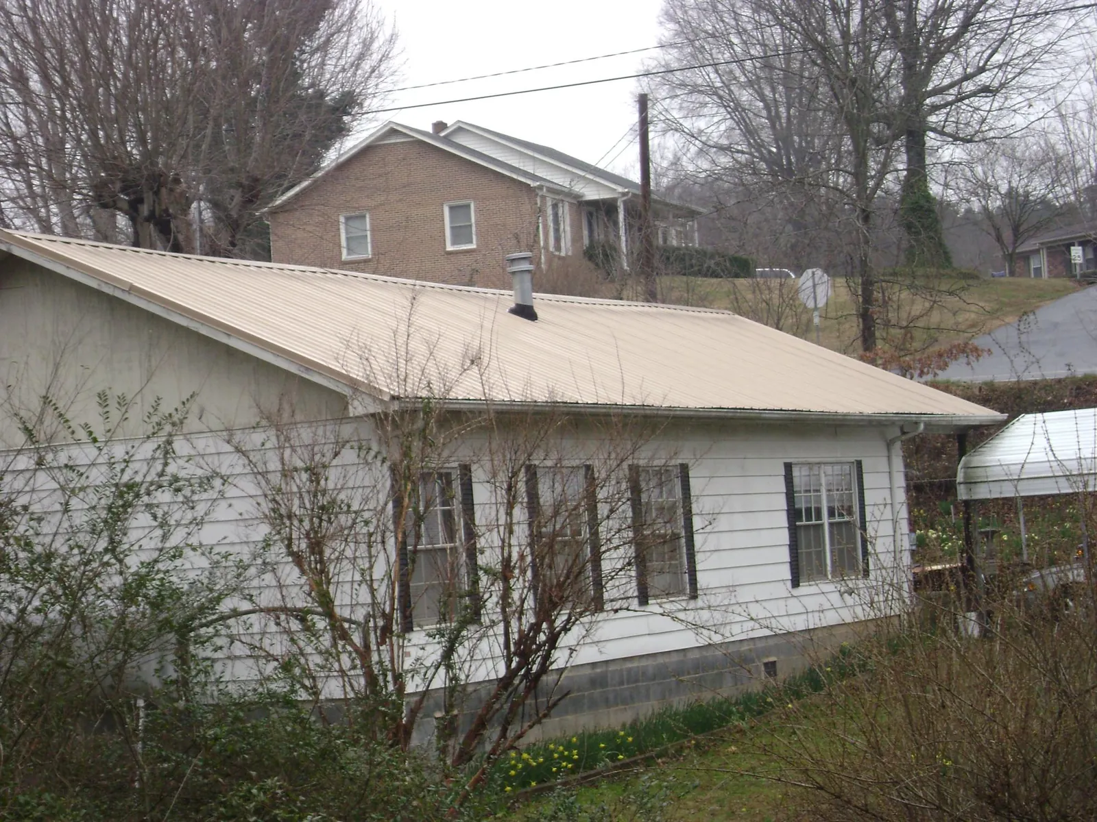 Tan metal roof on a white sided house set into a hillside — Commercial Roofing by Roofing Brothers in Silverton